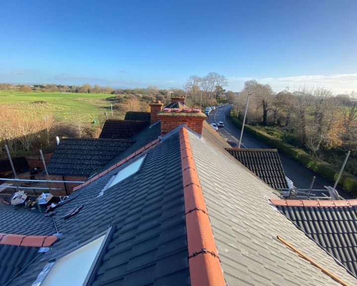 A new pitched roof with grey tiles and a clay tile ridge line installed on a residential building.