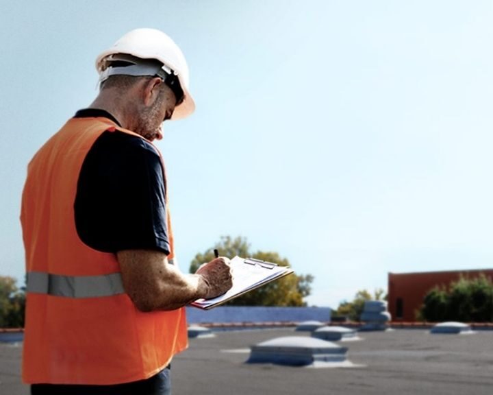 A roofer inspector taking notes on a clipboard whilst conducting a roof survey.